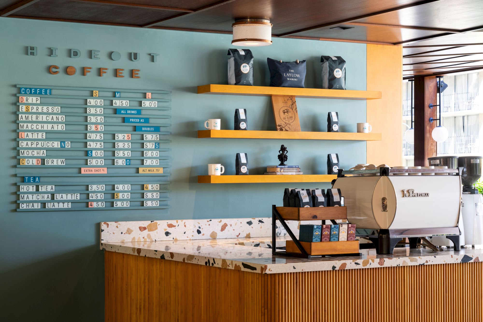 The image shows a coffee shop counter with a menu on the wall and a coffee machine on the counter.