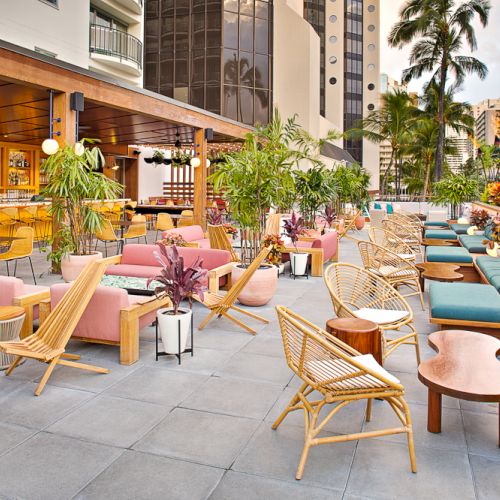The image shows an outdoor patio with wicker furniture, colorful cushions, plants, and a bar area, creating a relaxing atmosphere.